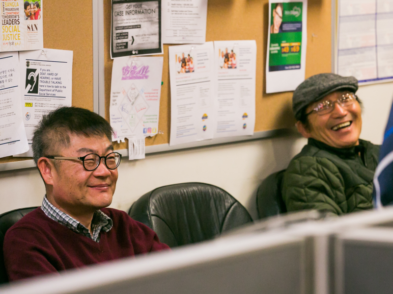 Elder Korean patients laugh together during a behavioral health referral visit, sharing a supportive moment with the provider.