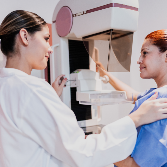 A patient receives a mammogram as a technician positions the breast imaging machine for screening.